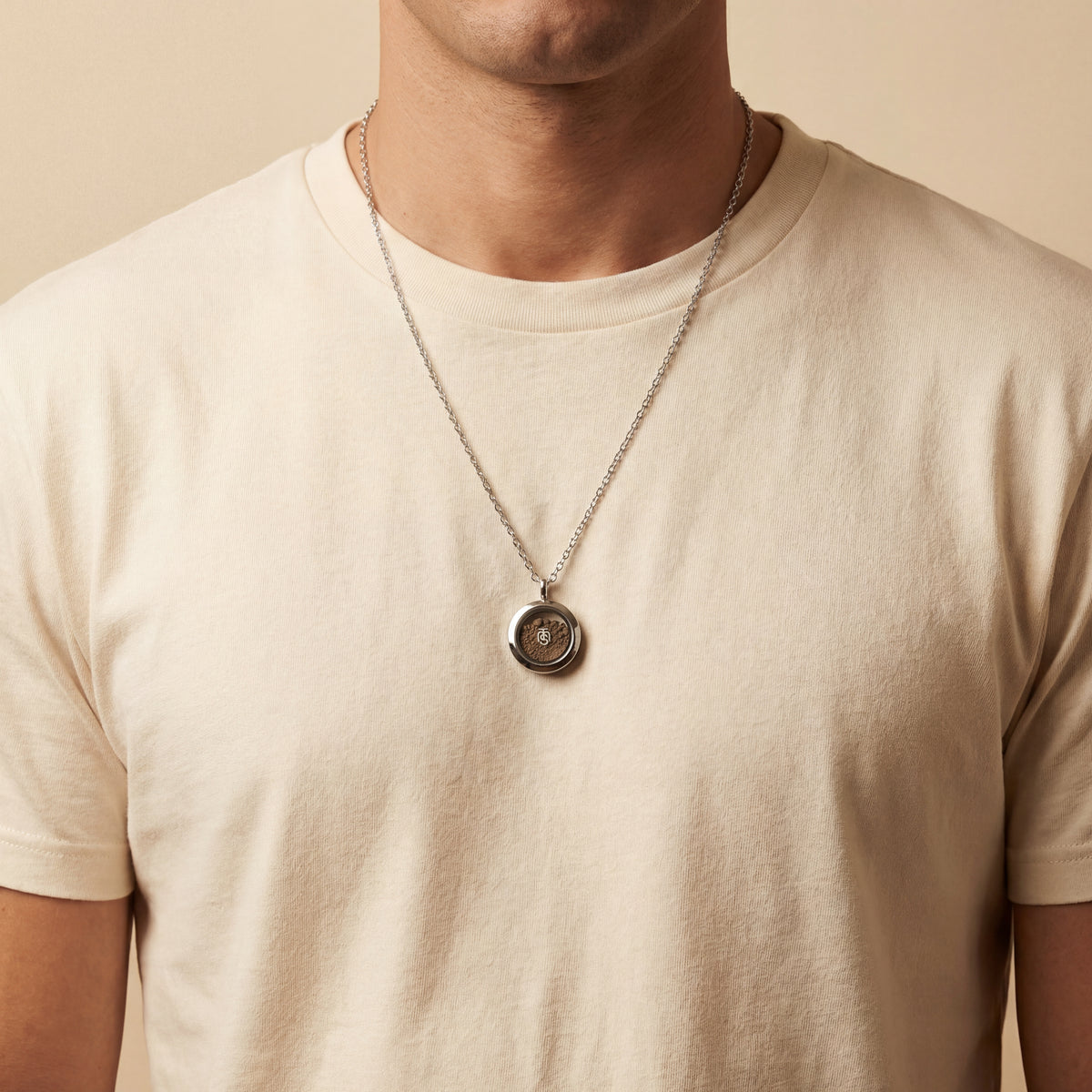 Silver Locket of Divine Promise worn on a chain over a cream t-shirt